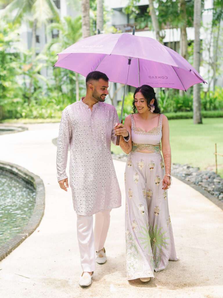 Luxury Indian wedding Bali couple walking together under umbrella at Conrad Bali garden