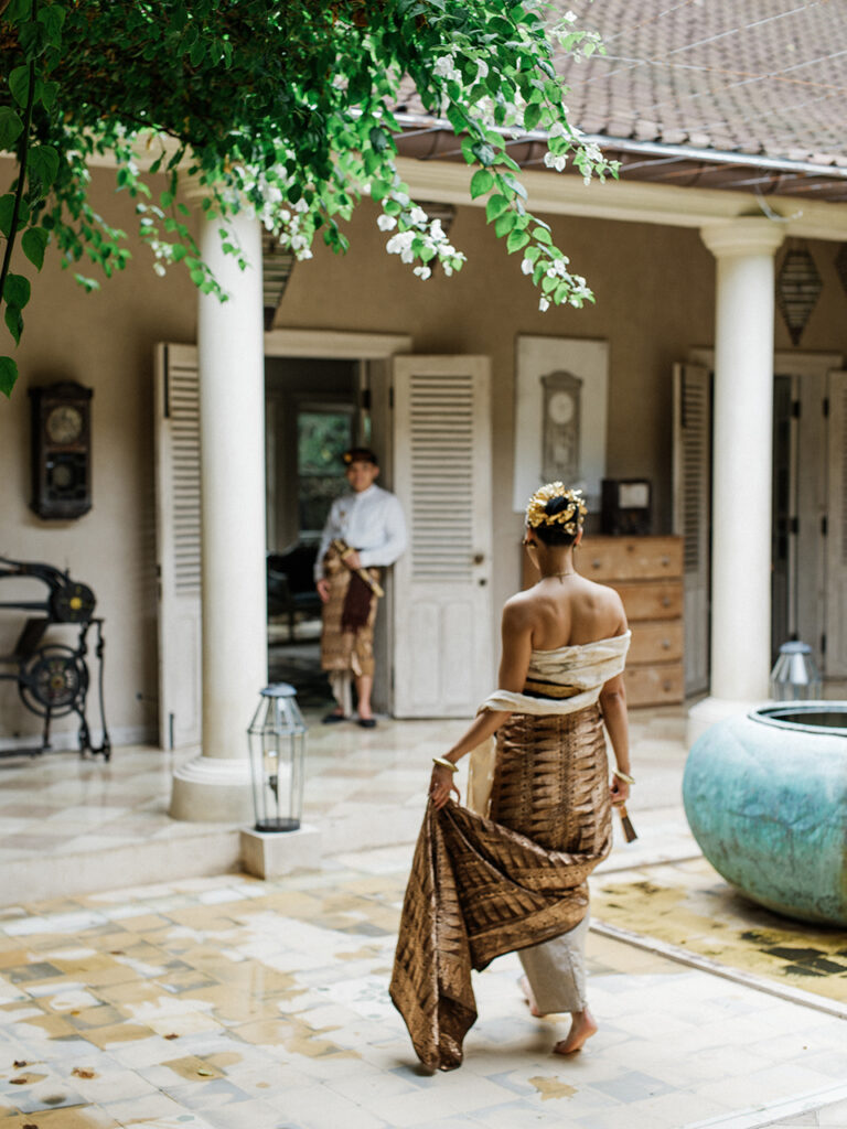 Bali couple photoshoot at Balquisse Heritage Hotel with bride in traditional Balinese outfit walking through an intimate courtyard setting