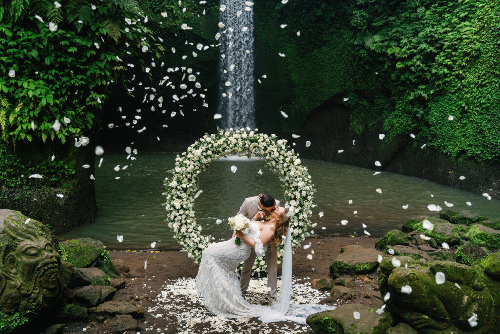 ubud waterfall elopement wedding couple kissing under floral arch bali intimate ceremony