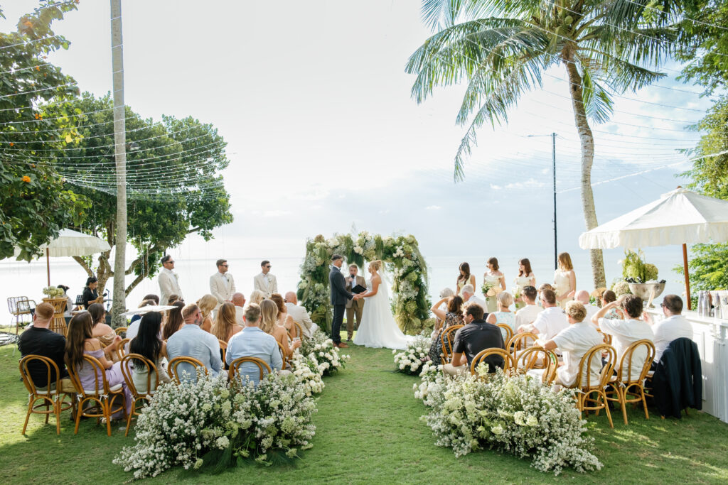 Villa Pemutih wedding Bali ceremony in Uluwatu with ocean view, bride and groom exchanging vows under floral arch during an intimate cliffside wedding