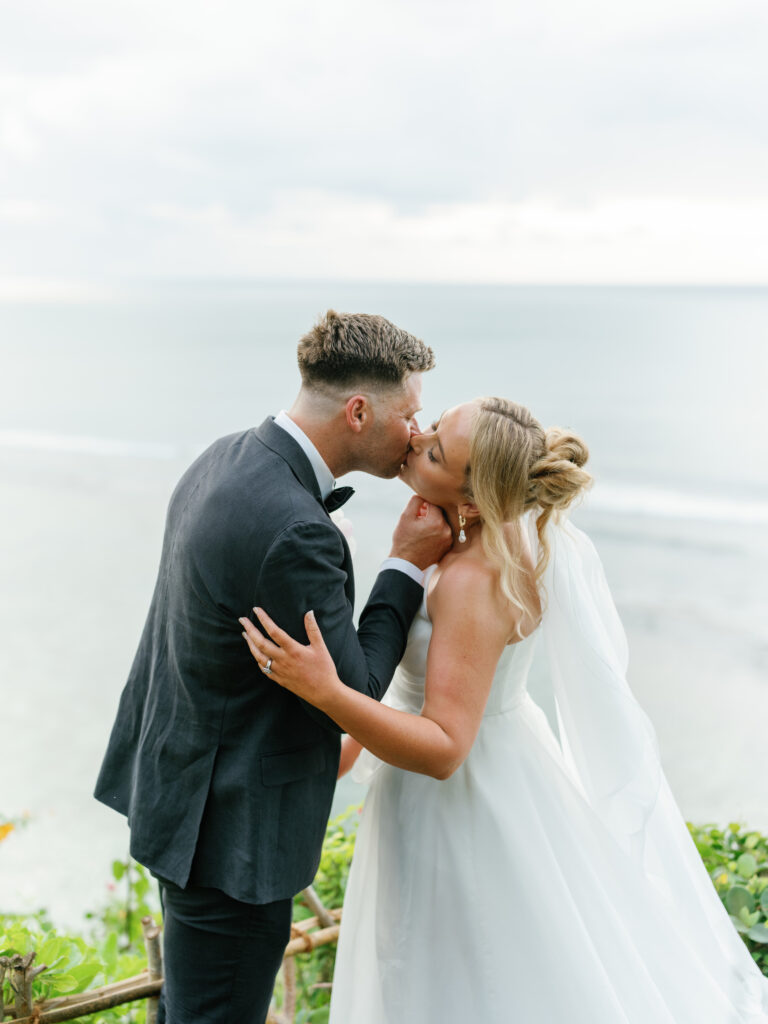 Bride and groom sharing a kiss during a cliffside portrait at Villa Pemutih Bali with ocean view in Uluwatu