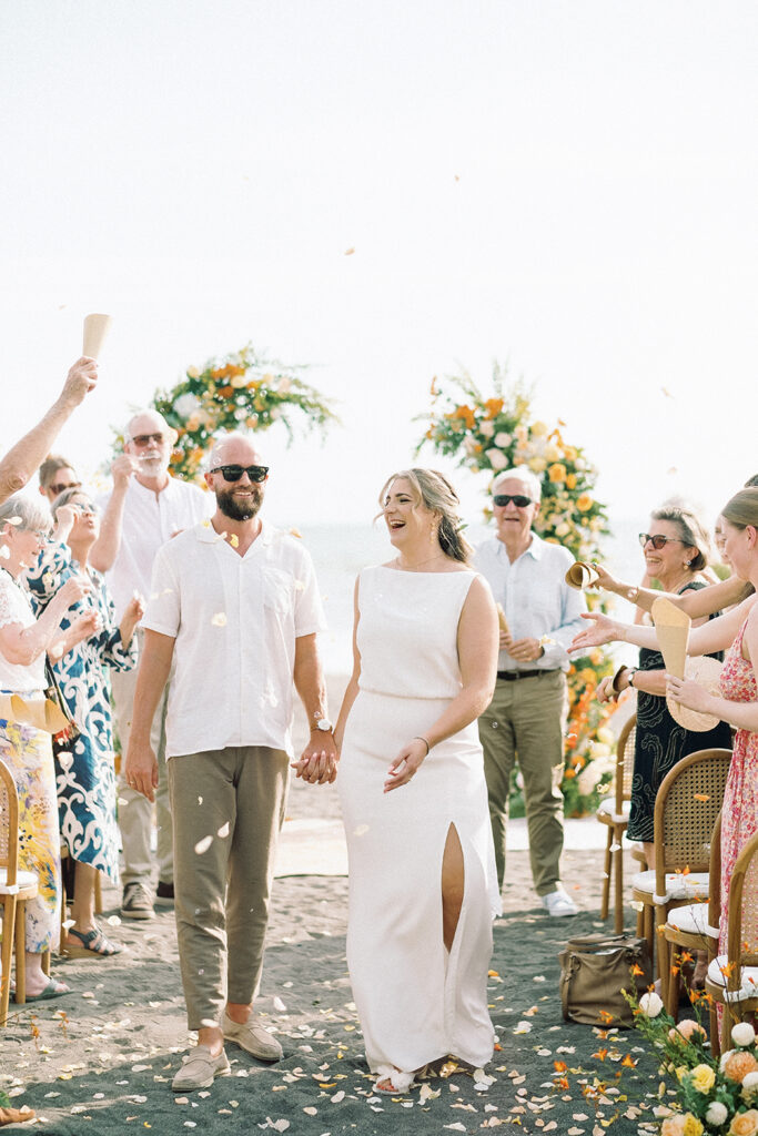 intimate elegant wedding in Bali couple walking down sandy aisle with guests throwing flower petals at Villa Vedas beach ceremony