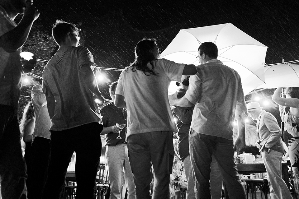 Wedding guests dancing in the rain at outdoor Bali reception — unplanned moment captured by documentary wedding photographer