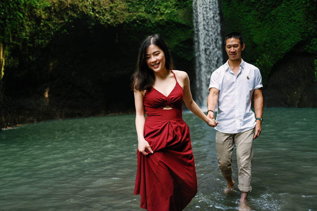 Couple walking through water at Tibumana Waterfall during a Bali 2 hour couple photoshoot in a lush jungle setting
