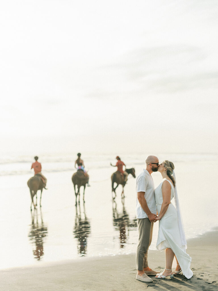 intimate elegant wedding bali couple portrait on beach at sunset with horse riders background