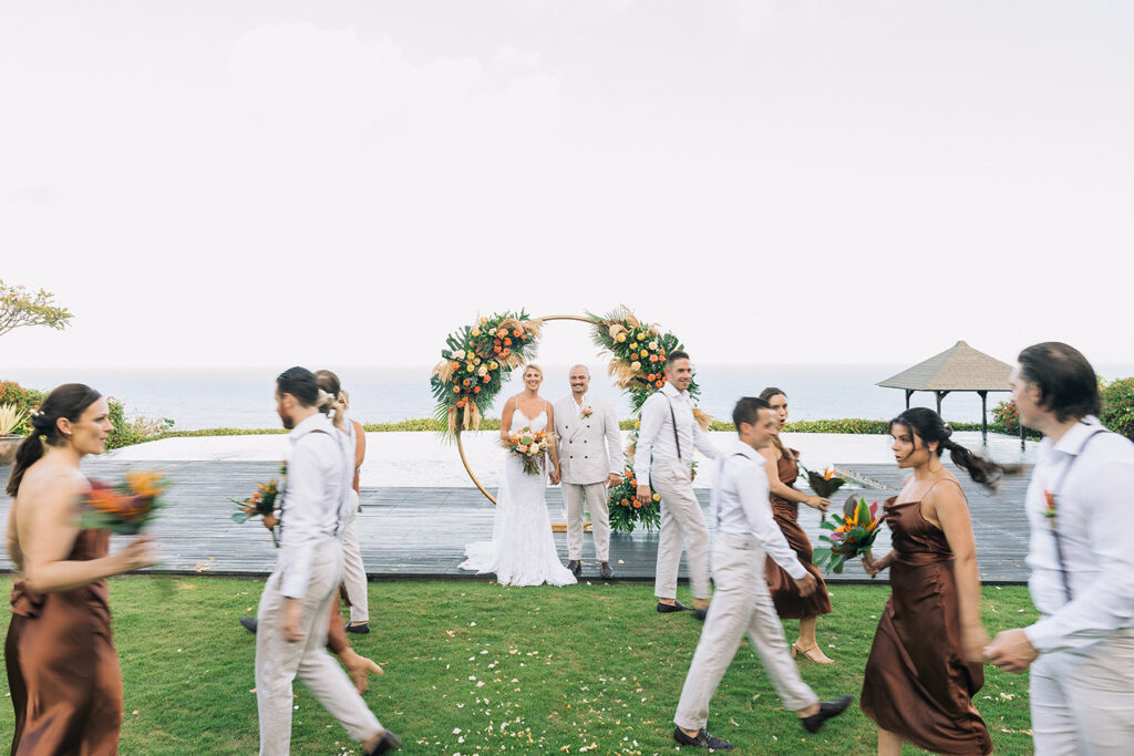 Aimee and Blake standing at the altar during their Bali wedding experience as guests walk around in a candid moment