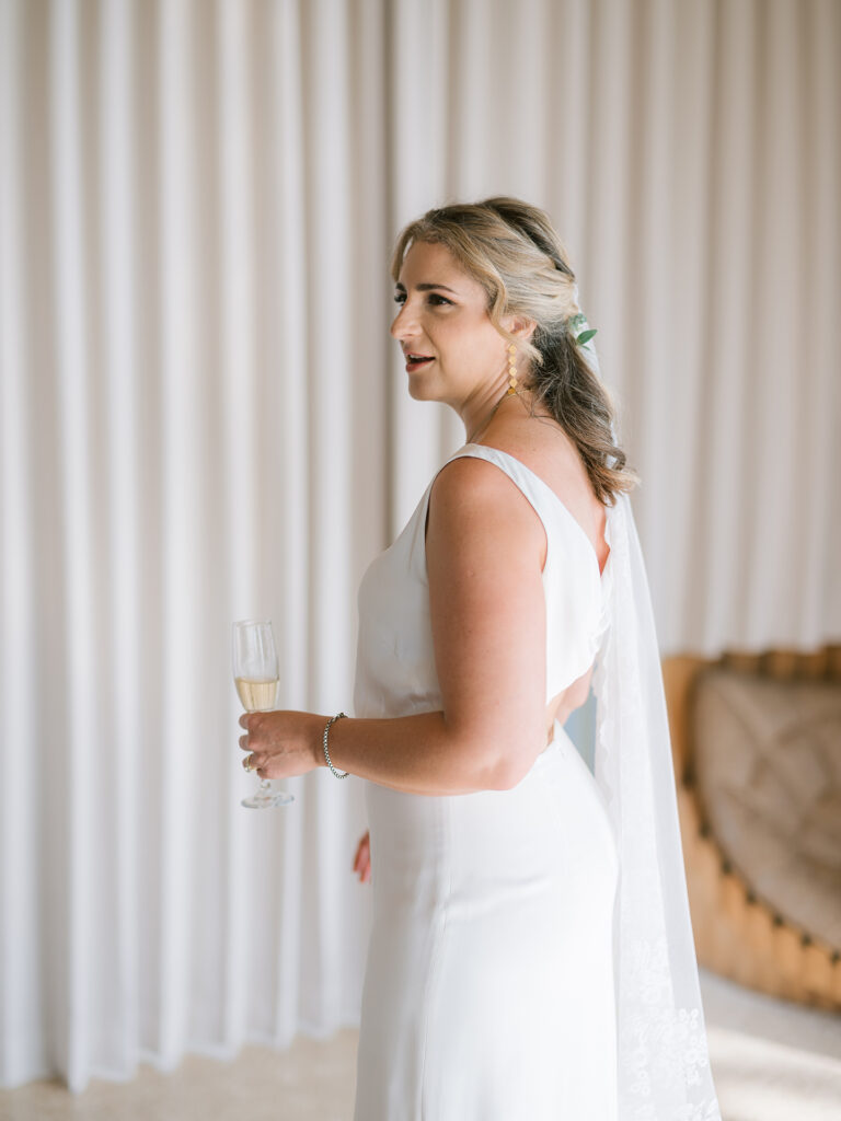 intimate elegant wedding in Bali bride holding champagne glass during preparation at Villa Vedas with soft natural light and minimal setting