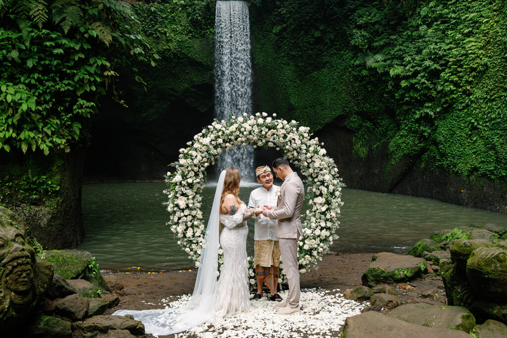 ibumana Waterfall elopement ceremony in Bali with couple and celebrant under floral arch