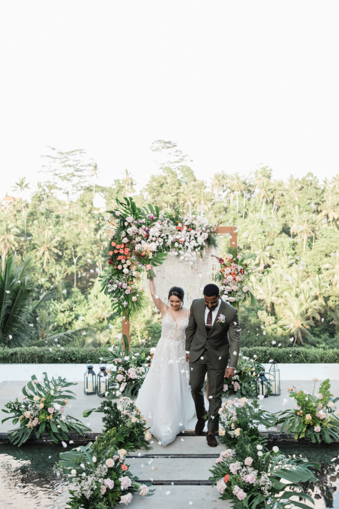 Ubud elopement couple walking after ceremony at Jannata Resort Bali with floral setup and falling petals
