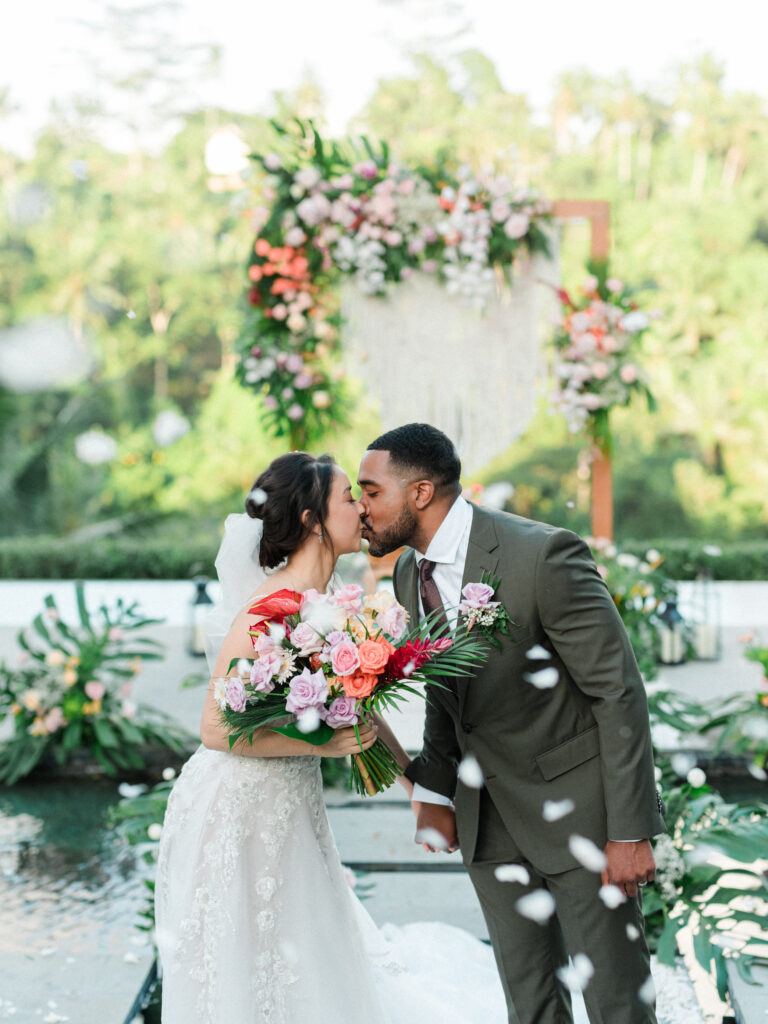 Ubud elopement couple kissing at Jannata Resort Bali with floral arch and falling petals