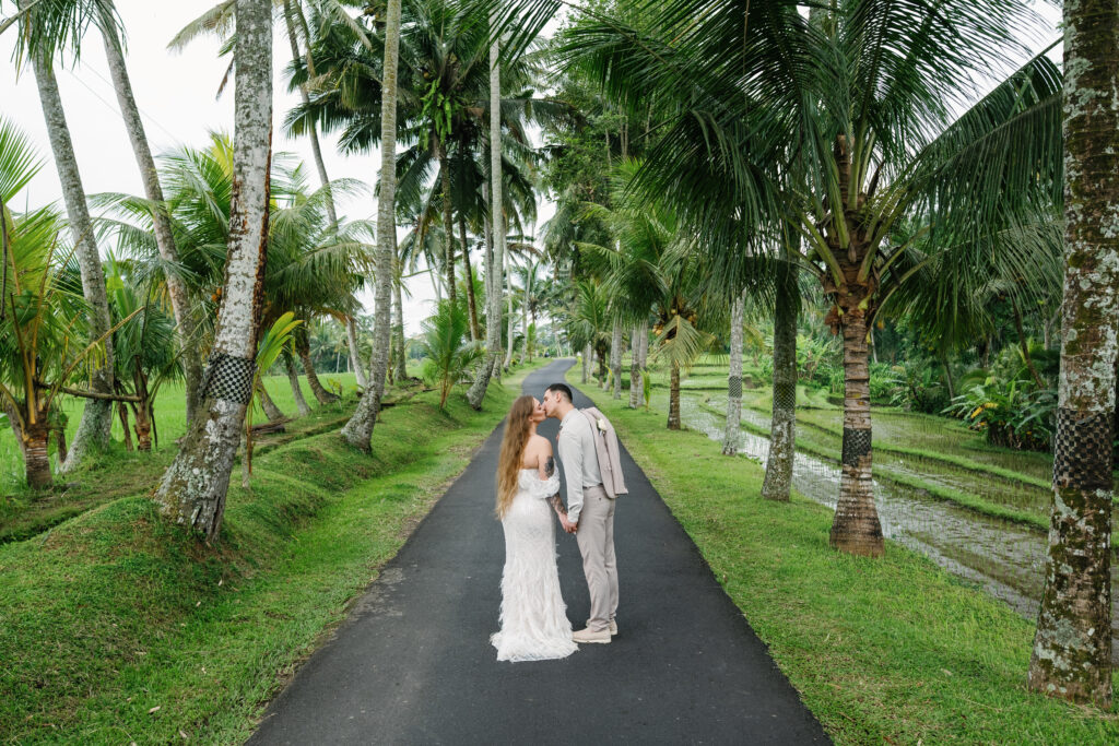 Couple kissing on tropical road surrounded by coconut trees during Bali elopement