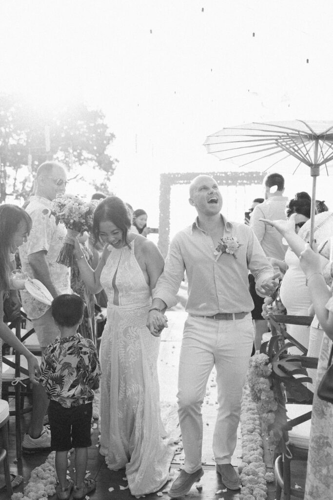 Bride and groom walking down the aisle after ceremony during a sunset wedding in Uluwatu Bali surrounded by guests celebrating