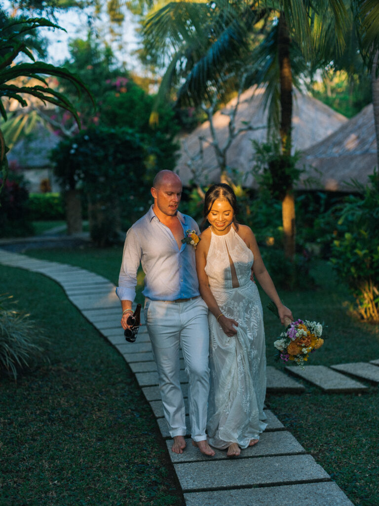 Bride and groom walking together during sunset in Uluwatu Bali through a tropical garden after their wedding ceremony