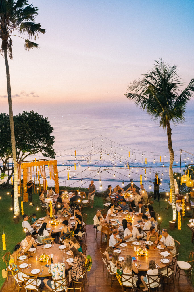 Uluwatu sunset wedding Bali reception with outdoor dinner setup, string lights and ocean view during evening celebration