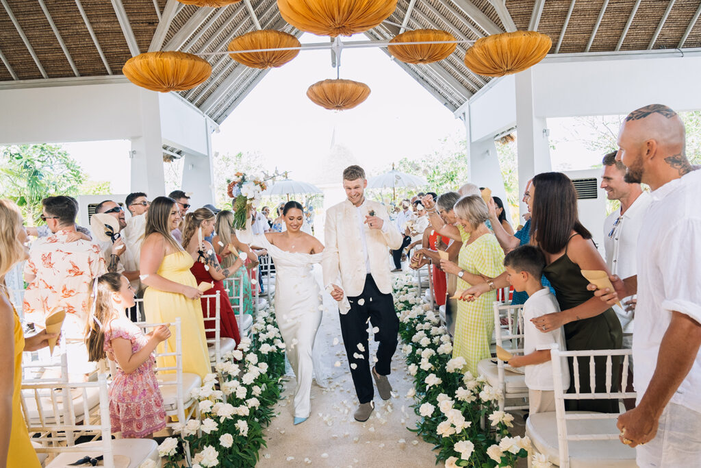 wedding ceremony exit at Puri Temple Hill chapel with guests and floral aisle Jimbaran Bali
