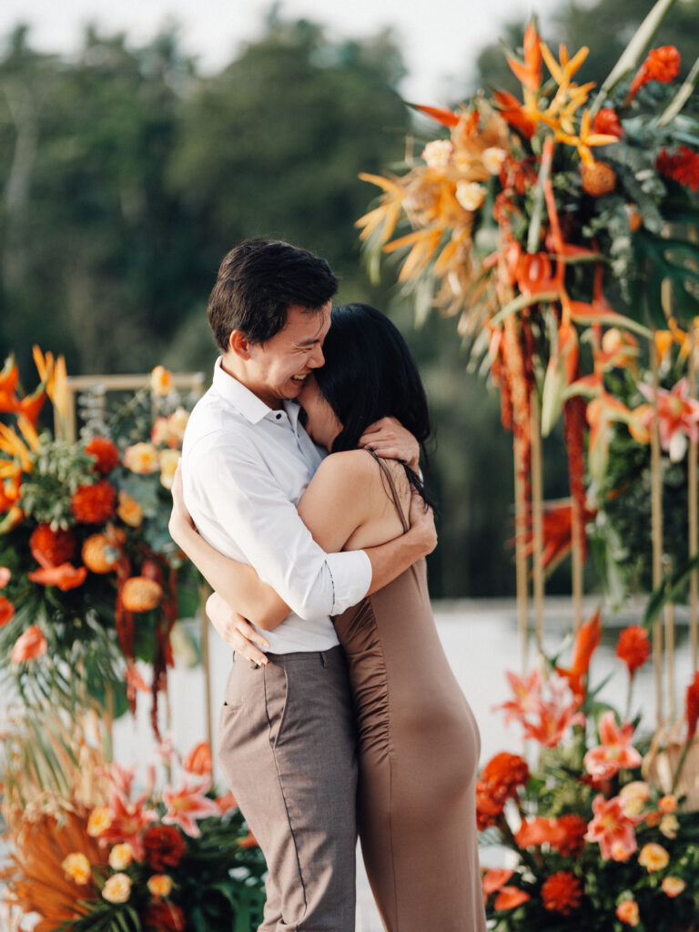 Emotional Bali proposal moment in Ubud with couple embracing surrounded by tropical flowers and lush jungle backdrop