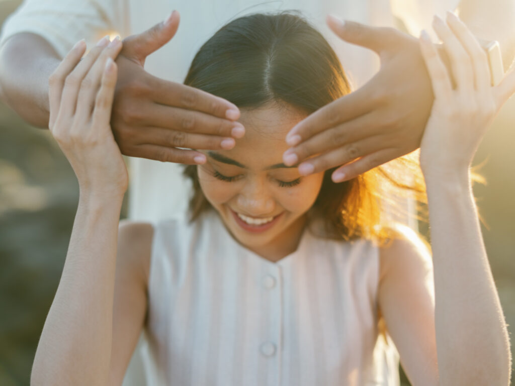 Playful Bali proposal moment with groom covering bride’s eyes during surprise engagement in warm sunset light