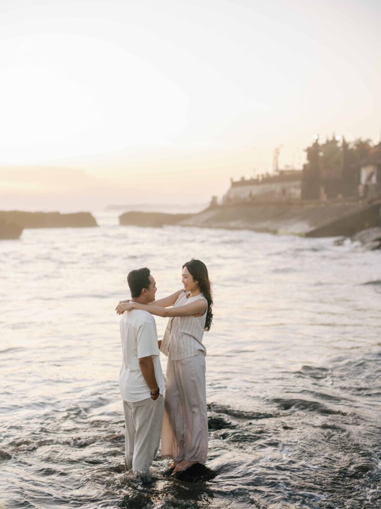 Honeymoon photoshoot Bali couple standing in the ocean at Echo Beach during golden hour, relaxed natural connection with soft light and waves.