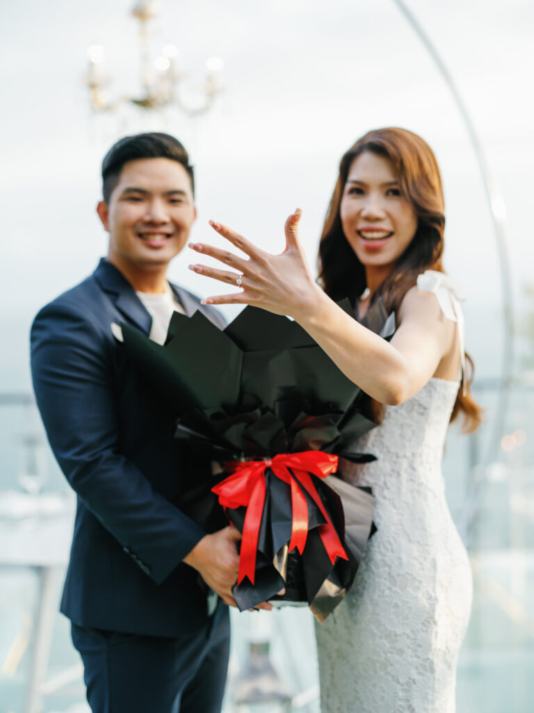 Happy couple showing engagement ring during Bali proposal photoshoot in Uluwatu, elegant bouquet and candid emotional moment