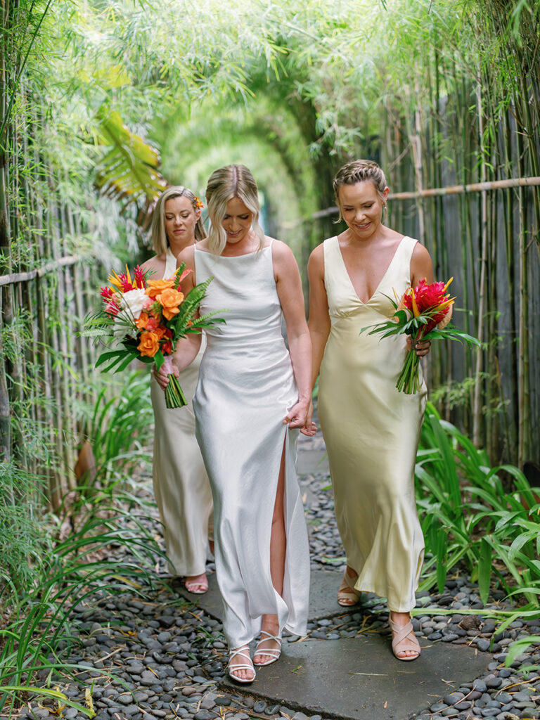 Alt: Bride and bridesmaids walking through bamboo corridor at Komune Resort Bali wedding
