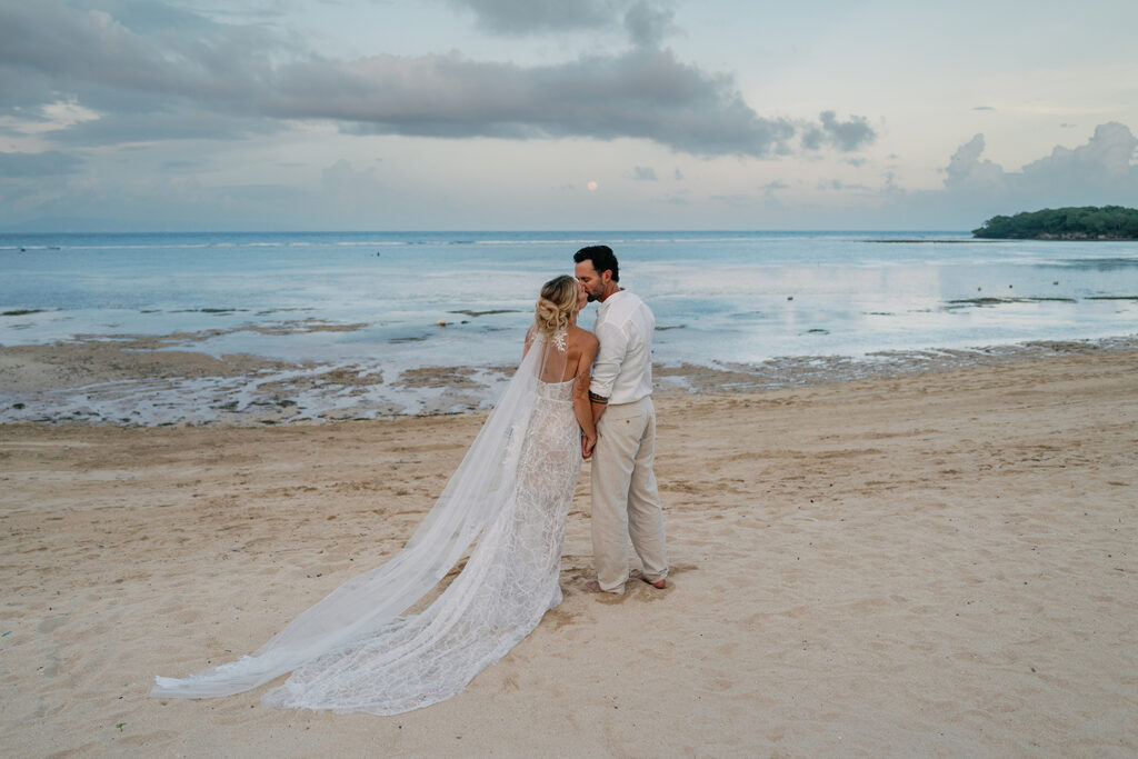Bride and groom sharing a kiss on the beach at sunset during their Bali destination wedding