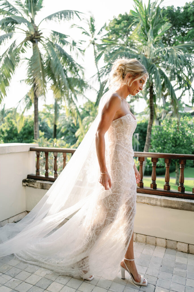 Getting Ready — Bride portrait on balcony Alt text: Bride in strapless lace wedding gown on hotel balcony surrounded by palm trees at Nusa Dua Beach Hotel Bali — Luxima Wedding photography