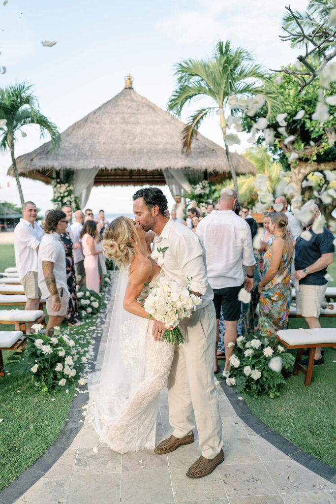 Ceremony — First kiss with petal toss Alt text: First kiss at Nusa Dua Beach Hotel wedding ceremony with guests throwing petals Bali — Luxima Wedding photography