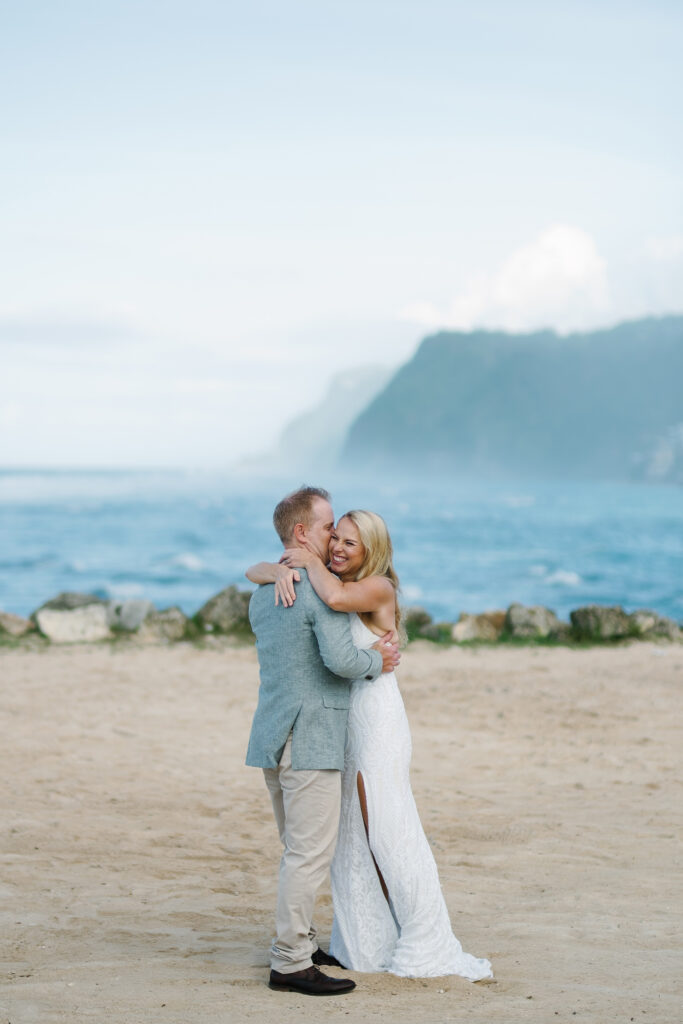Bride and groom embracing on Melasti Beach after elopement ceremony with limestone cliffs behind — Luxima Wedding