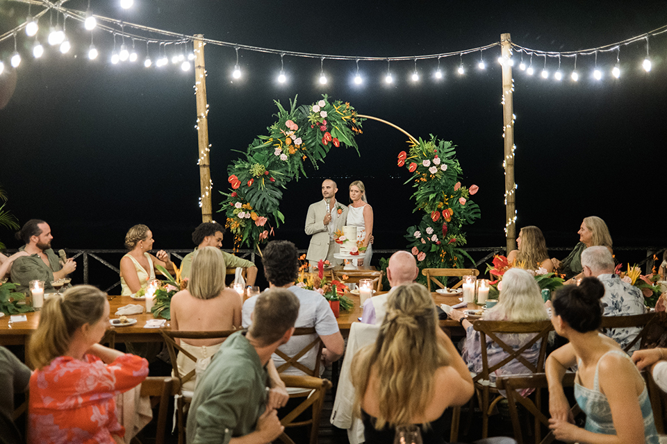 Alt: Outdoor wedding reception at Komune Resort Bali with tropical floral arch and ocean backdrop