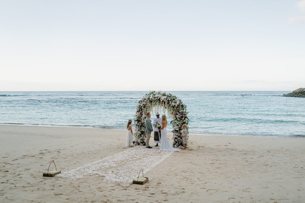 Melasti Beach elopement ceremony with floral arch at sunrise — Luxima Wedding Bali