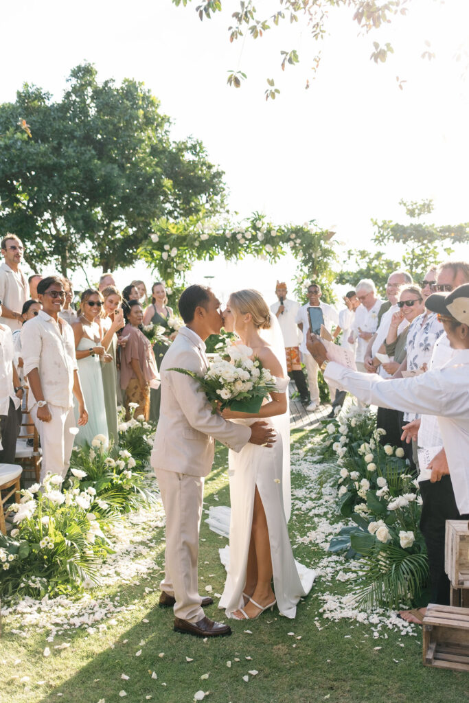 First kiss wedding ceremony Padma Resort Legian Bali with guests and tropical floral arch