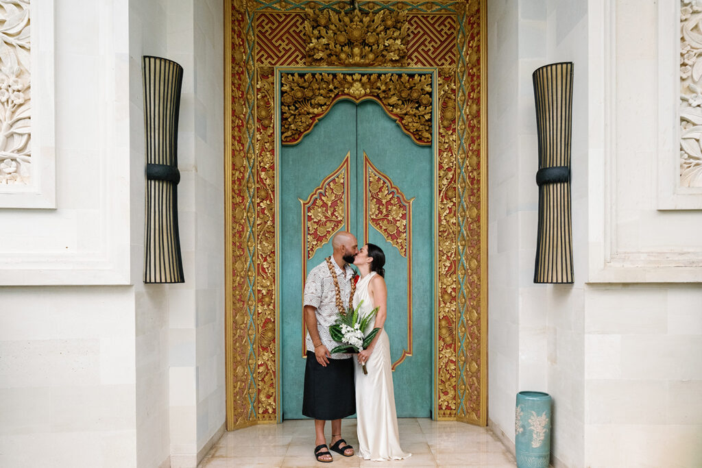 Bride and groom kissing in front of an ornate Balinese carved door during their Bali wedding