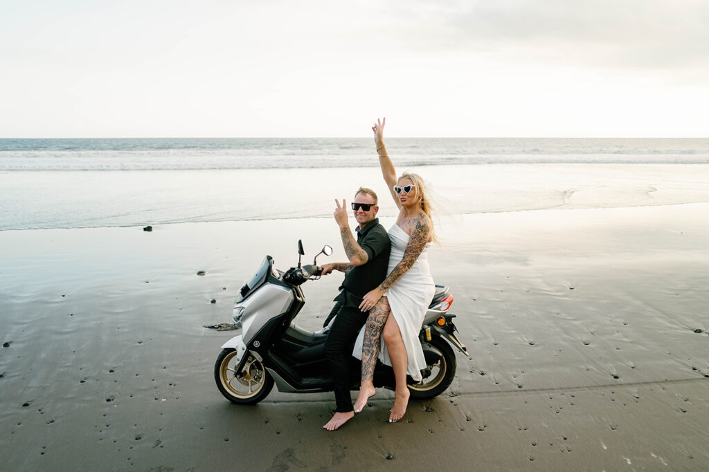 Kaytie and Jamie on scooter at Pasut Beach during vow renewal Bali peace sign celebration — Luxima Wedding