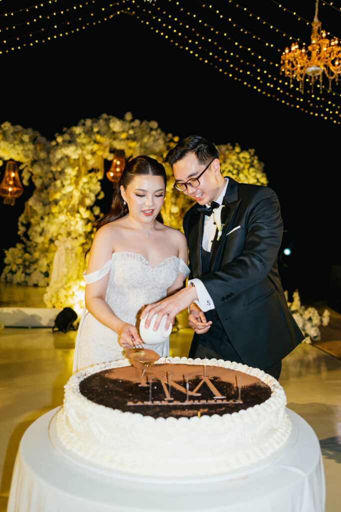 Randy and Michelle cutting wedding cake at Villa Plenilunio Uluwatu night reception with fairy lights and chandeliers — Luxima Wedding