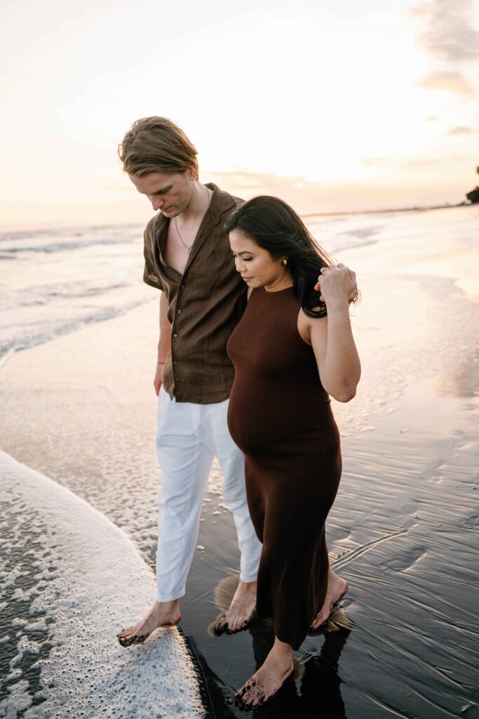 Tom guiding Elly through tide at Nyanyi Beach Bali maternity session sunset