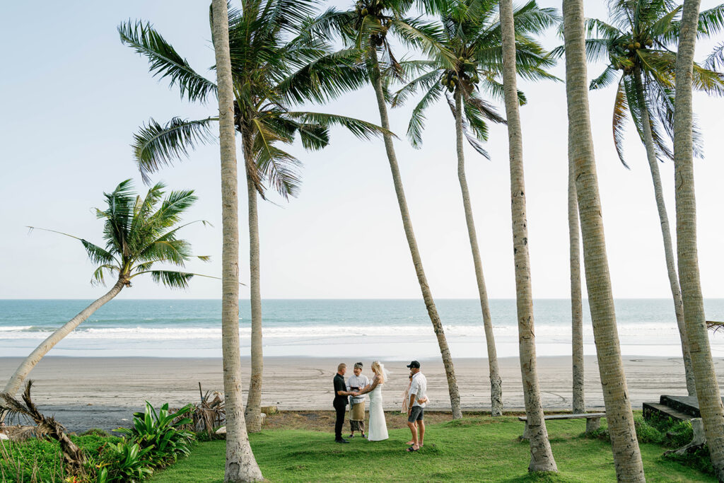 Kaytie and Jamie walking hand in hand through tropical palm grove during Bali vow renewal — Luxima Wedding