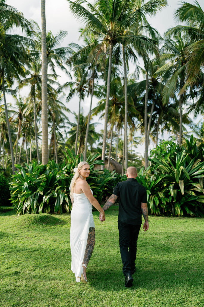 Kaytie and Jamie walking hand in hand through tropical palm grove during Bali vow renewal — Luxima Wedding