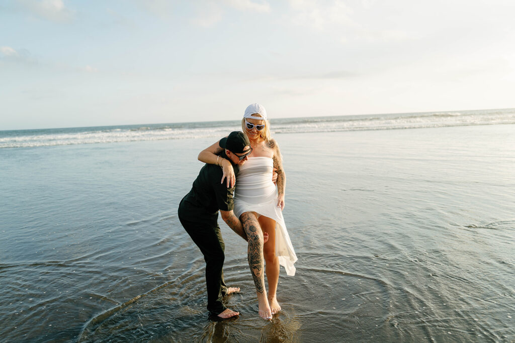 Jamie and Kaytie laughing together at the waterline during intimate vow renewal Bali beach session — Luxima Wedding