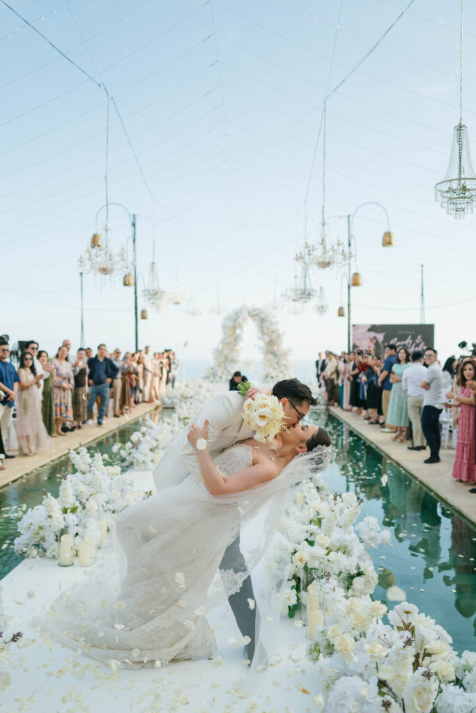 Randy dipping Michelle for a kiss on the pool aisle recessional at Villa Plenilunio Uluwatu with guests celebrating — Luxima Wedding