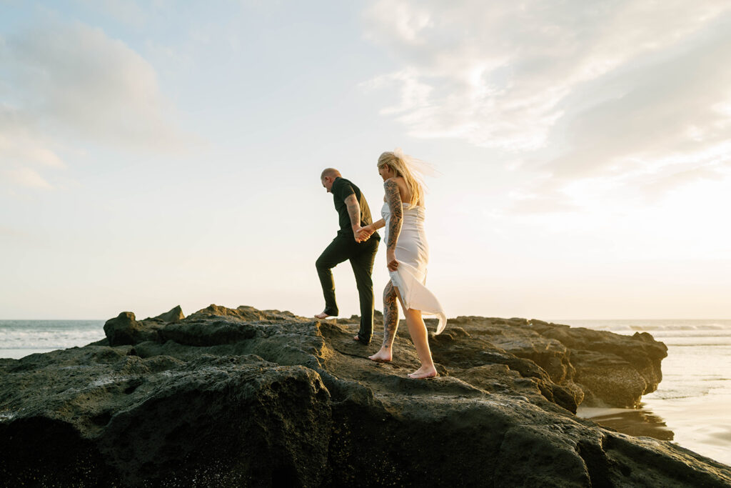 Jamie leading Kaytie over coastal rocks at golden hour during Bali vow renewal photography — Luxima Wedding