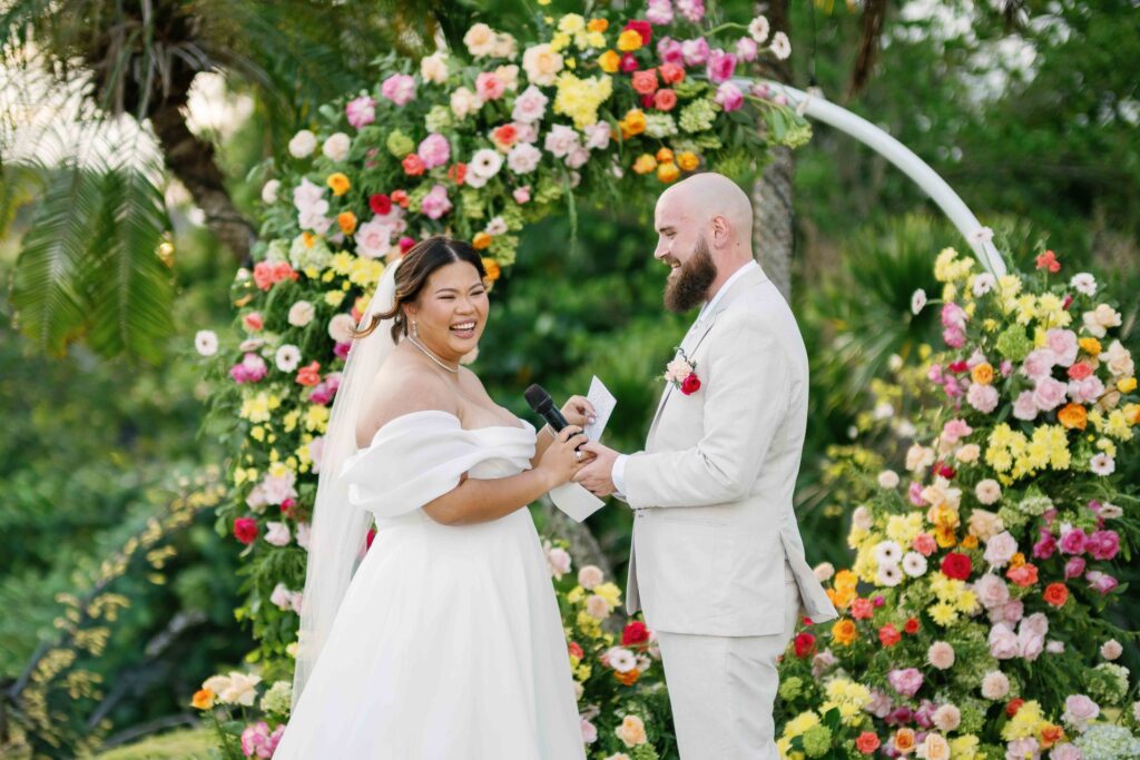 Janela and Jack exchanging vows under colourful floral arch at Peppers Seminyak Bali wedding